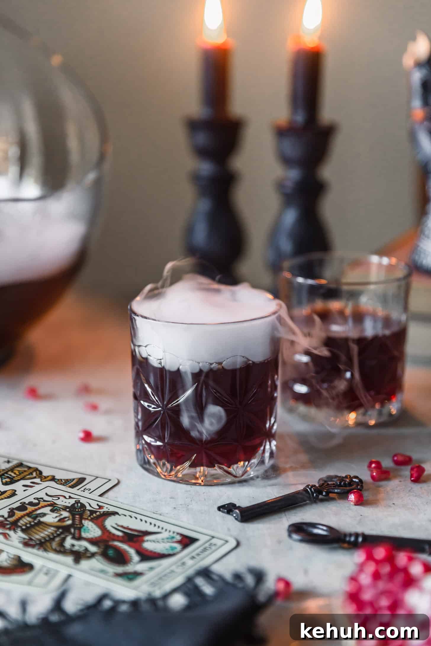 Spooky Witches Brew Punch Recipe for Halloween Parties 8 Two witches brew cocktails on a grey table next to black candles, pomegranate arils, vintage keys, and cards.