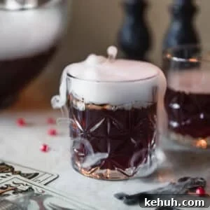 Spooky Witches Brew Punch Recipe for Halloween Parties 9 A purple cocktail with smoke on a white counter next to a punch bowl, vintage key, and cards.