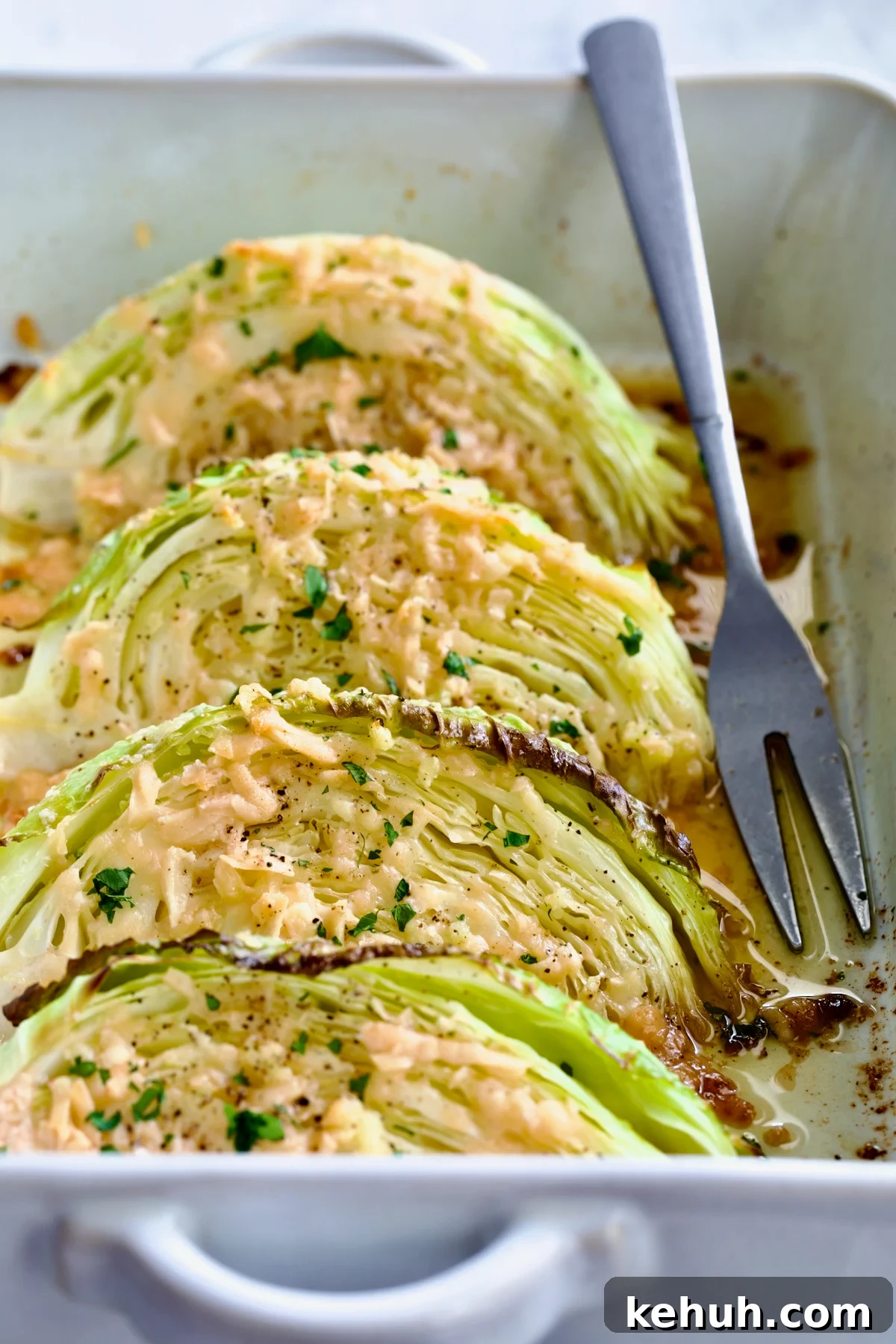 Baked Garlic Parmesan Cabbage Wedges in white baking dish with serving fork.