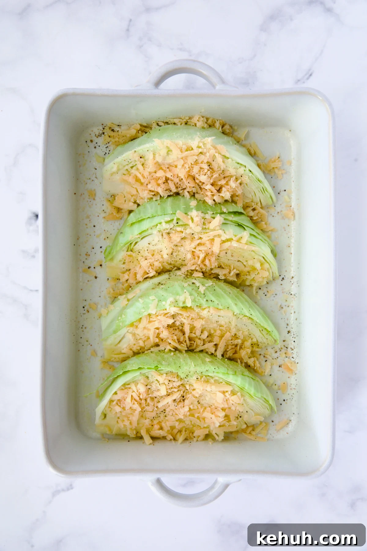 Four wedges of cabbage in white rectangular baking dish sprinkled with Parmesan cheese.
