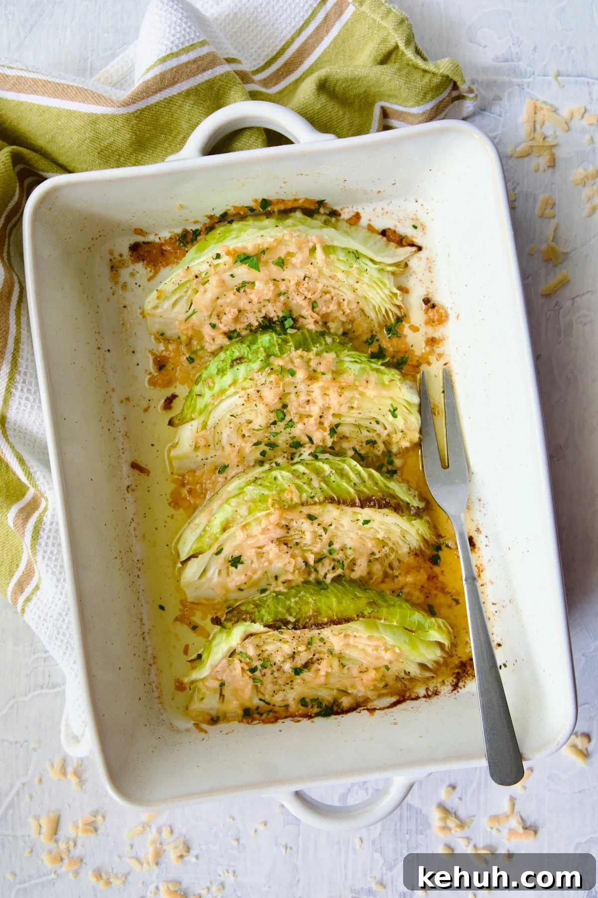 Baked Garlic Parmesan Cabbage Wedges in white rectangular baking dish with serving fork and green striped towel.