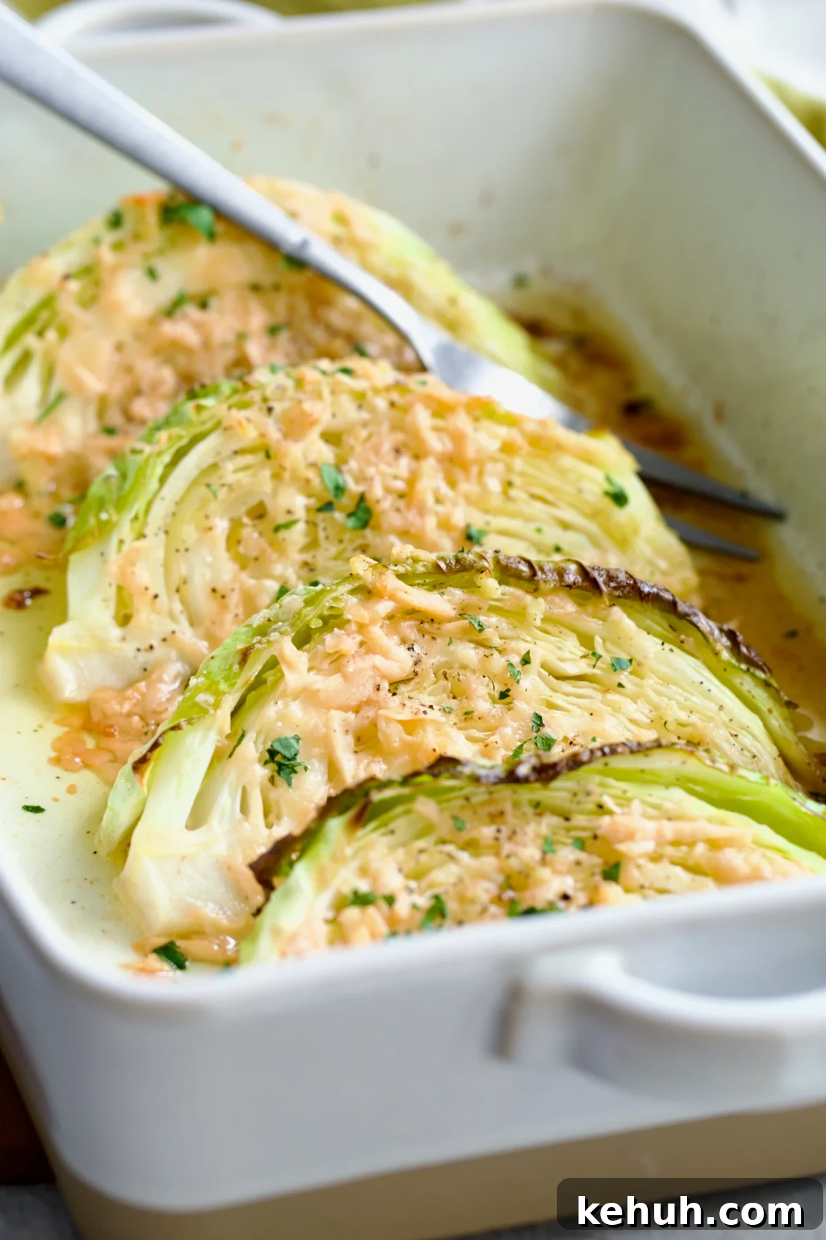 Four wedges of Baked Garlic Parmesan Cabbage Wedges in baking dish with serving fork garnished with fresh chopped parsley.