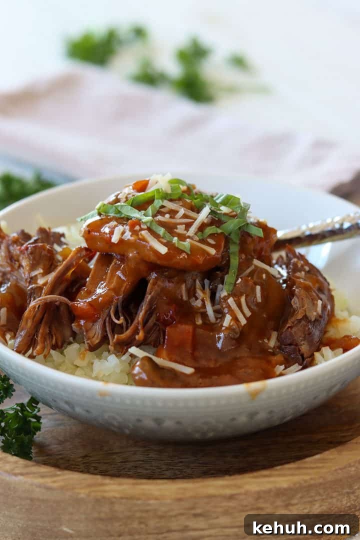 Juicy Ninja Foodi Pot Roast Recipe for Tender, Flavorful Beef 2 Portrait image of pressure cooker pot roast served in a gray and white bowl. Pot roast is shown served over cauliflower rice and garnished with parmesan cheese and basil.