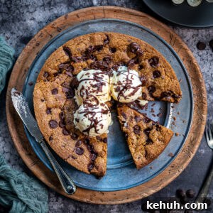 Giant Chocolate Chip Cookie Recipe — Air Fryer or Oven 10 A giant chocolate chip biscuit topped with three scoops of vanilla ice cream and chocolate drizzle sits on a plate. One slice is cut and slightly pulled out; a knife and chocolate chips are nearby.
