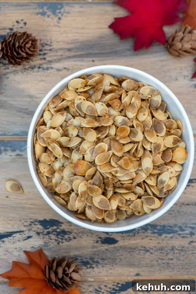 Crispy Roasted Acorn Squash Seeds Recipe 2 A top down shot of a bowl of roasted acorn squash seeds on a brown ball with fall leaves and pine cones.