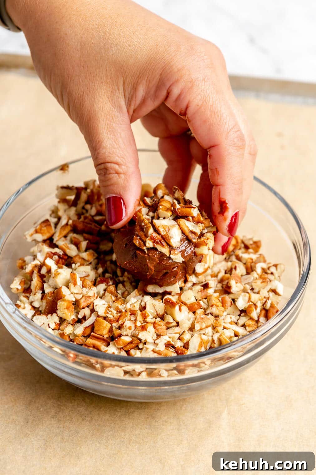 220824_Bourbon Pecan Truffles-15 Hand rolling bourbon ball in a bowl of pecans.