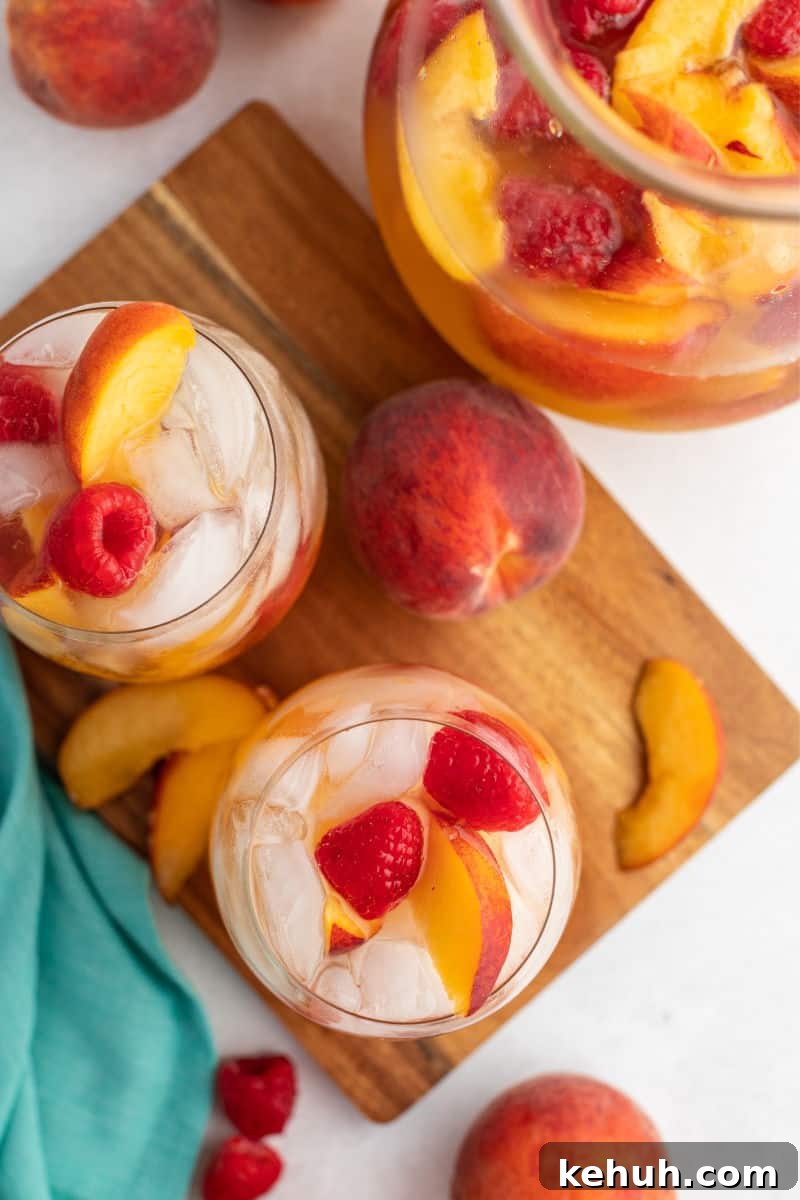 Bring on a never-ending pitcher of this Raspberry Peach Moscato Punch! Some wine, Sprite, and lots of fruit is a crazy good combo made for sharing! looking down at glasses of peach moscato punch on a cutting board