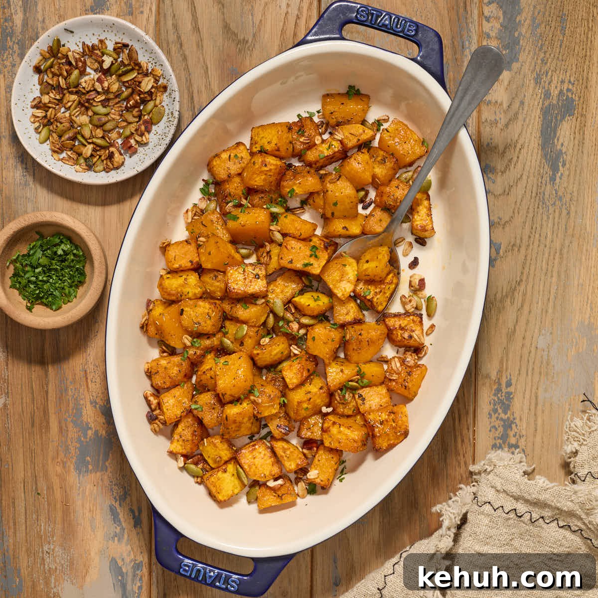 Air fryer butternut squash cubes in a serving dish with chopped pecans, pumpkin seeds and fresh herbs.