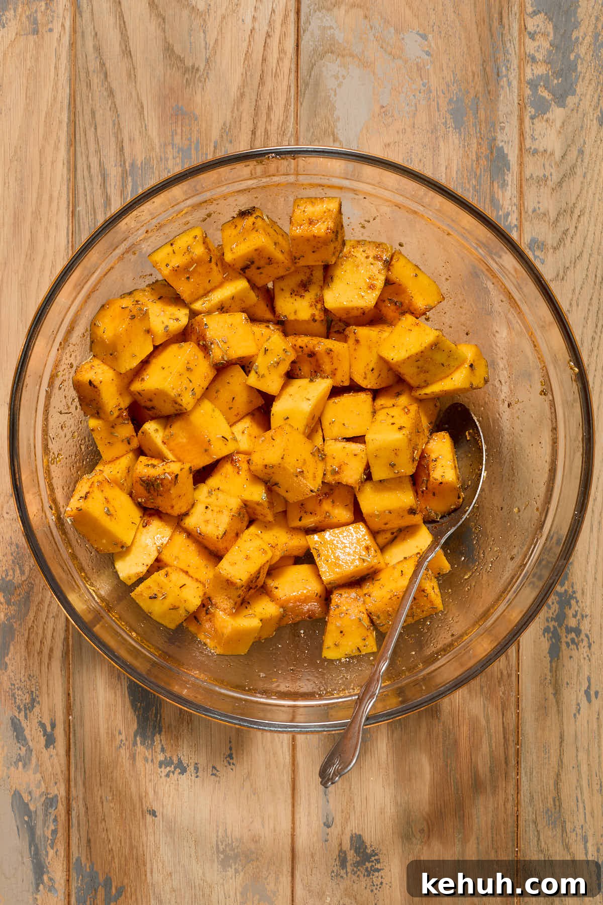 Squash cubes tossed with seasonings in a glass bowl.