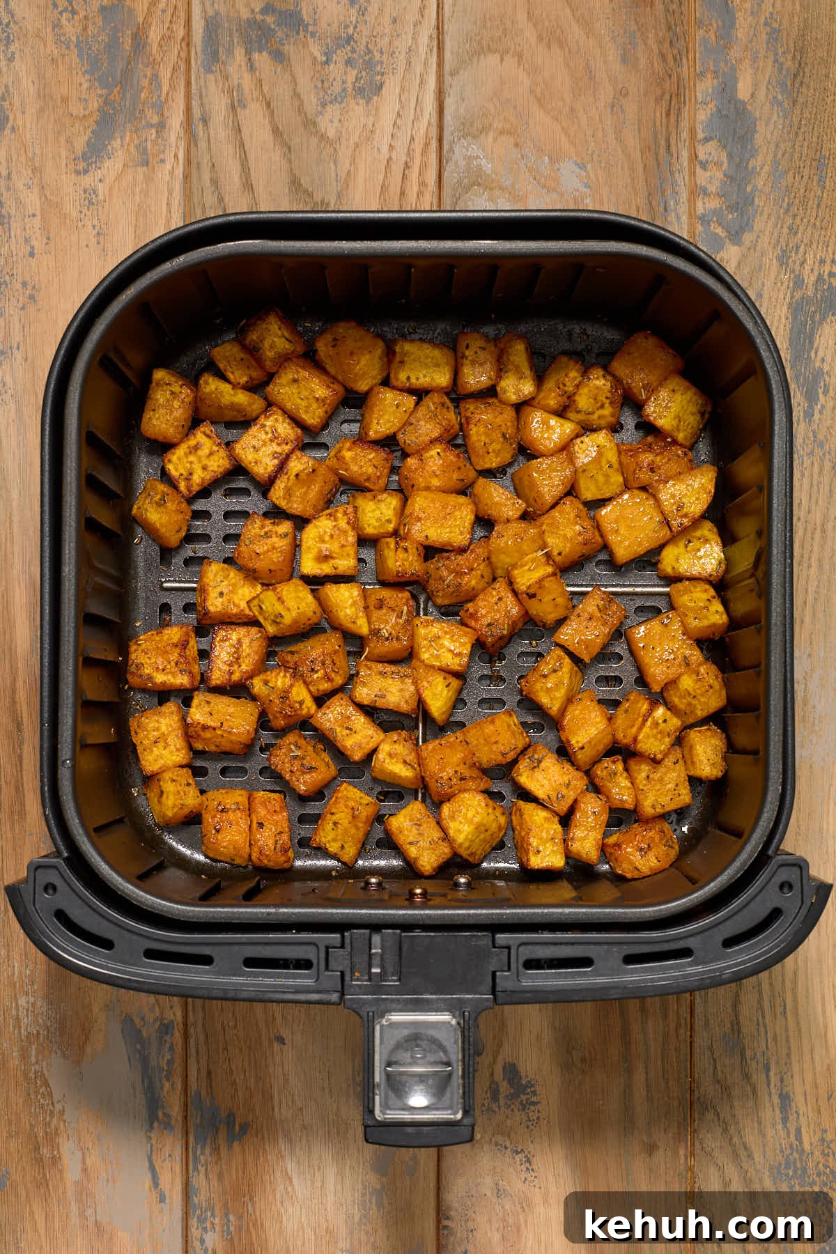 Air fried butternut squash cubes in an air fryer basket.