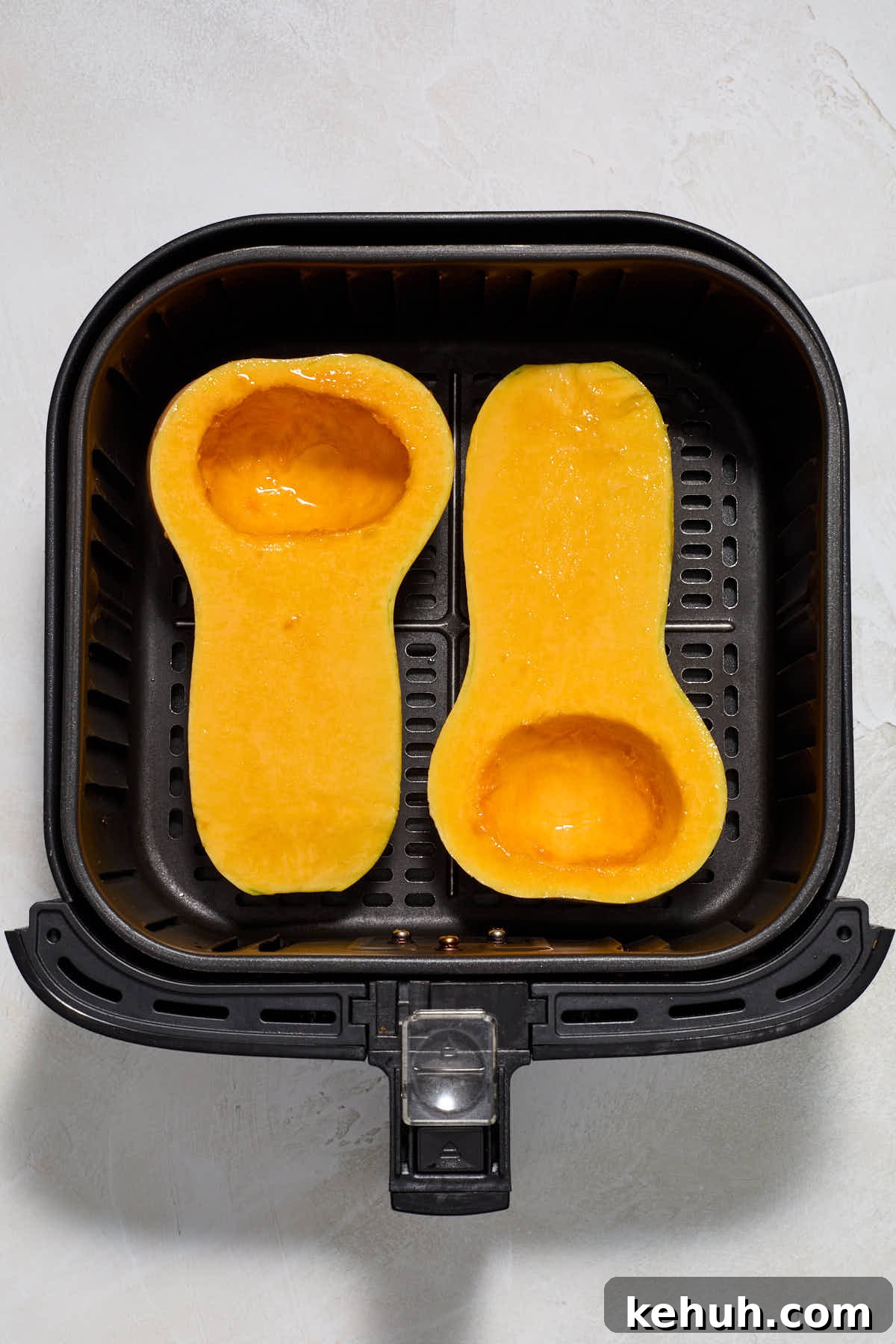 Butternut squash halves brushed with oil and arranged in air fryer basket.