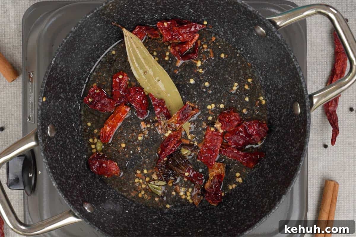 Crushed spices, bay leaf and dry red chilies added to hot oil in a pan.