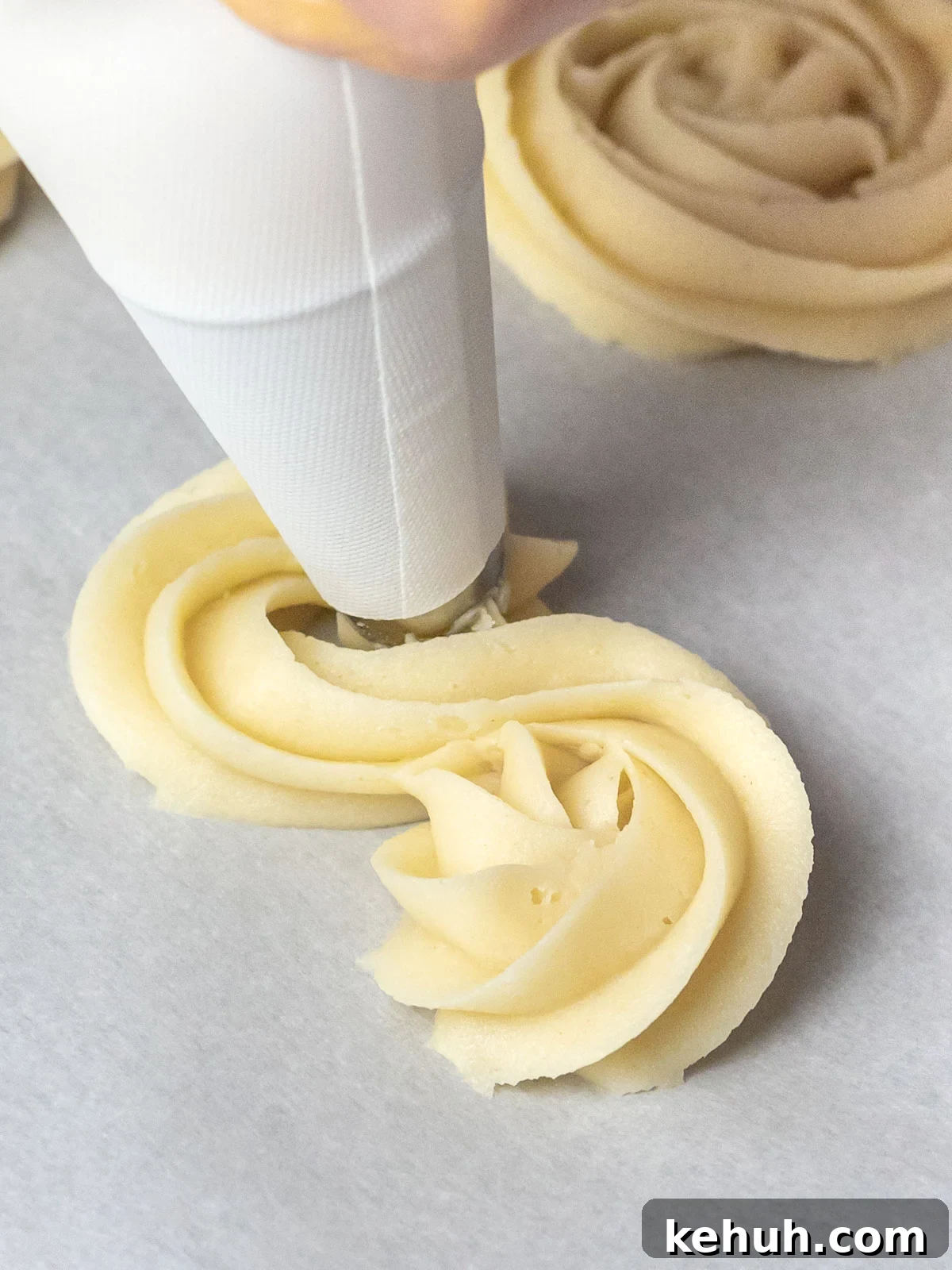 Classic Butter Cookies: Simple 6-Ingredient Recipe 5 butter cookies being piped with a piping bag onto parchment paper