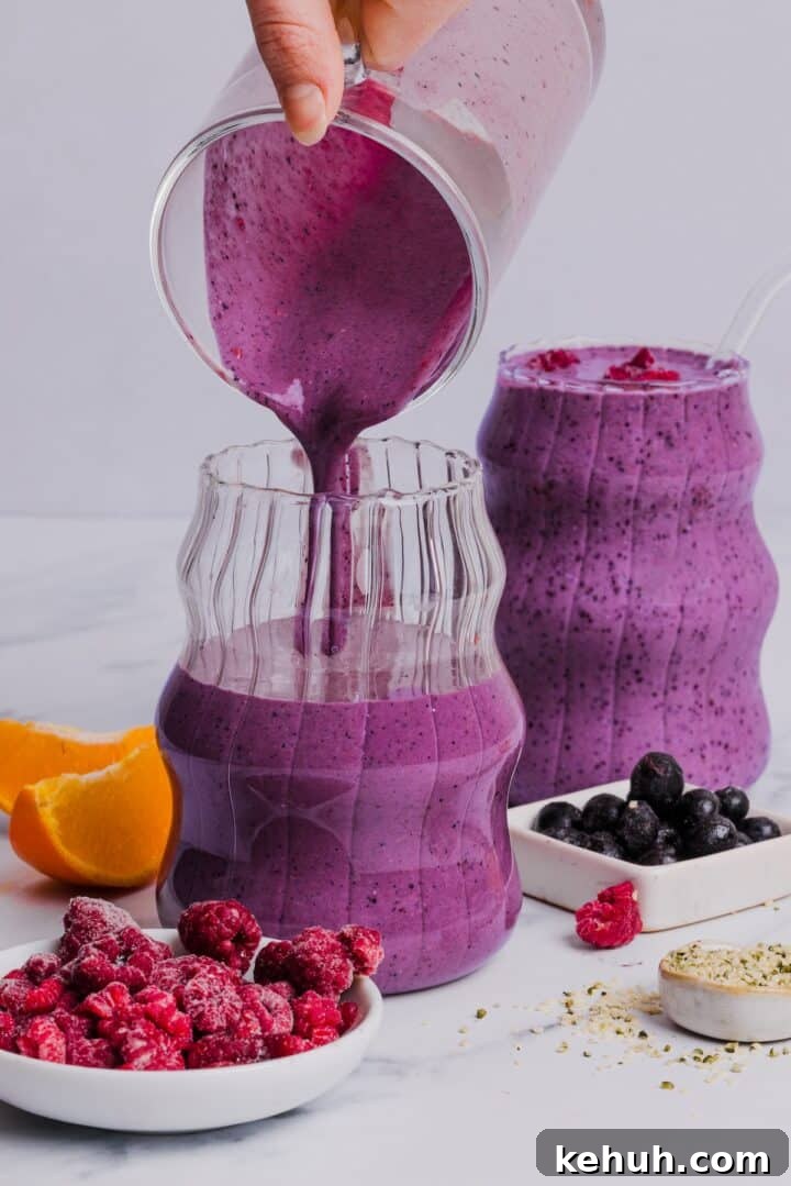 Blended blueberry raspberry smoothie being poured into etched glass