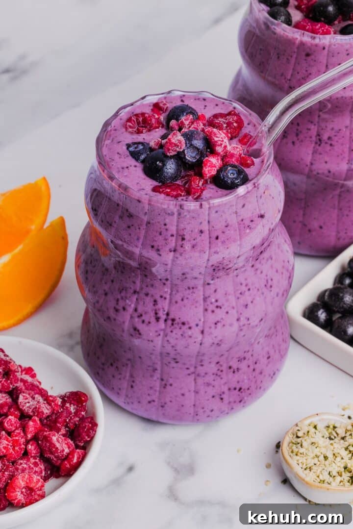 Close-up photo of two glasses with blueberry raspberry smoothie topped with frozen fruit