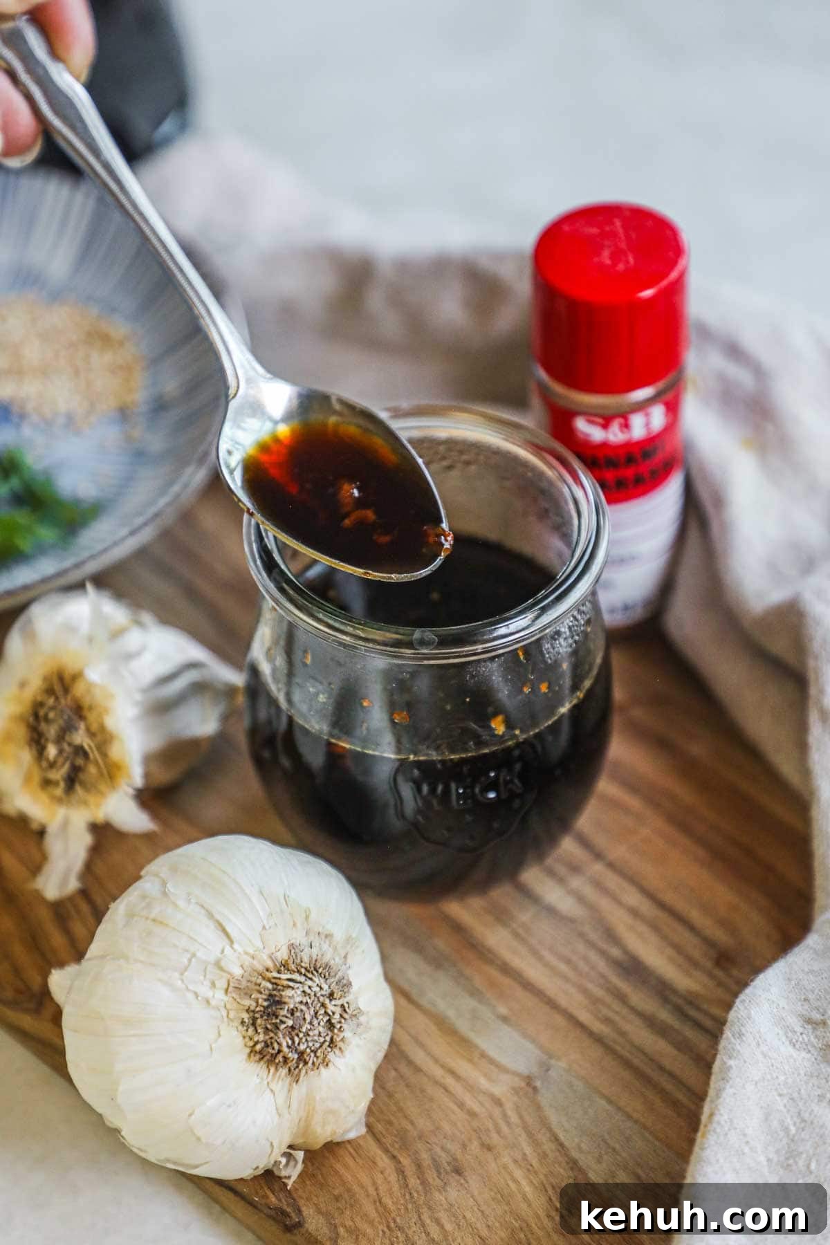 Spoon holding honey soy garlic sauce above a jar, to be used for chicken, fish, tofu, vegetables, and more.