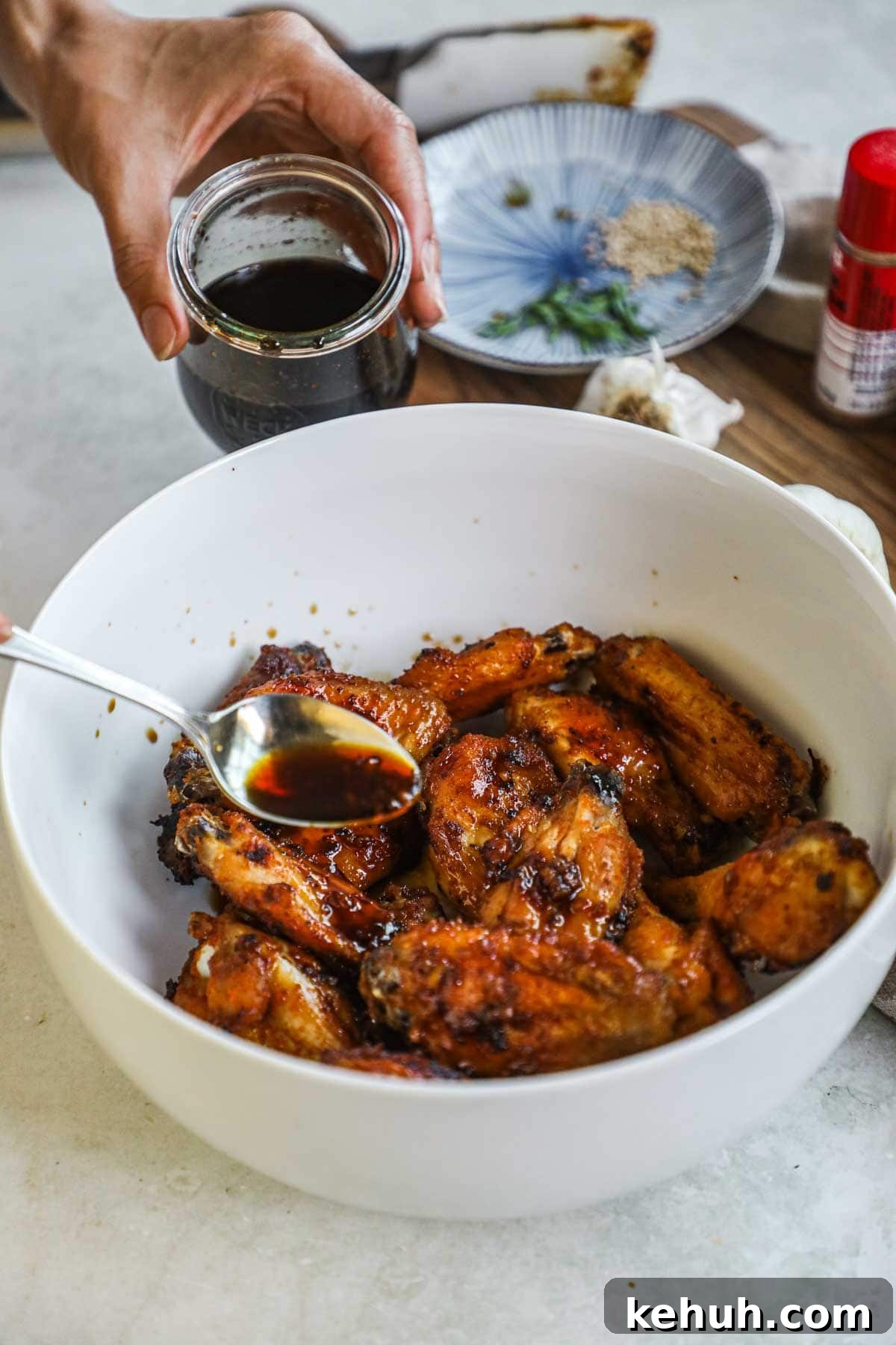 Spoon pouring honey soy garlic sauce on top of cooked wings to make a sticky, umami-packed glaze.