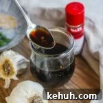 Spoon holding honey soy garlic sauce above a jar, to be used for chicken, fish, tofu, vegetables, and more.