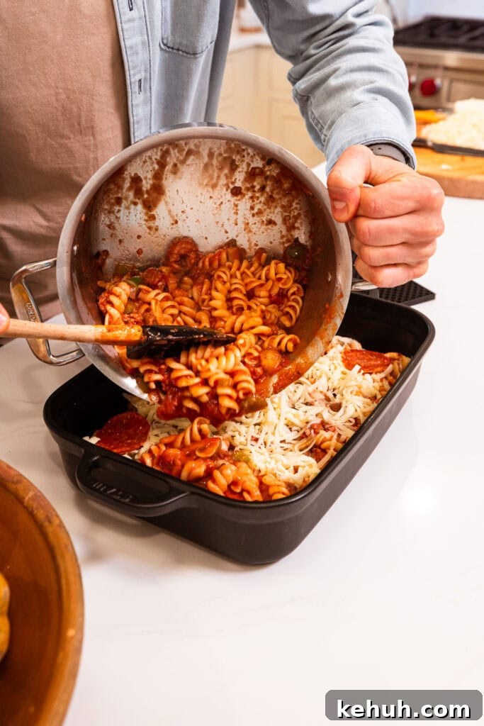 Cheesy Pizza Casserole Recipe with Sausage and Peppers 11 Pouring a pasta mixture into a baking dish.