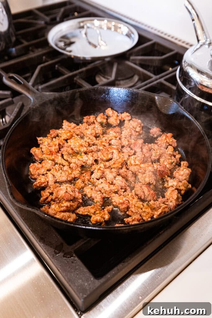 Cheesy Pizza Casserole Recipe with Sausage and Peppers 7 Sausage browns in a skillet on a stove.