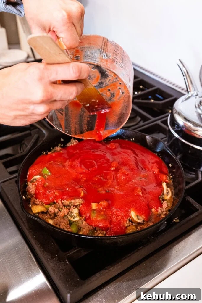 Cheesy Pizza Casserole Recipe with Sausage and Peppers 9 Strained tomatoes get added to a sausage and vegetable mixture on the stove.