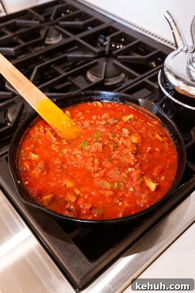 Cheesy Pizza Casserole Recipe with Sausage and Peppers 10 Sausage cooks in tomatoes on the stove.