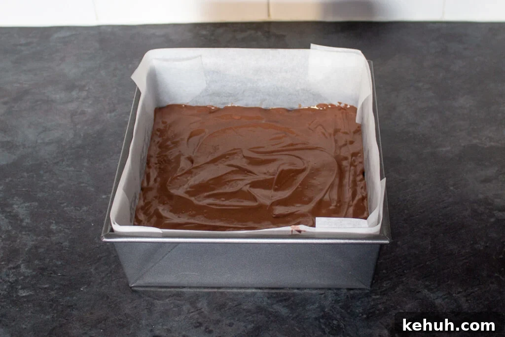 Melted milk chocolate smoothed over the top of a melted Mars Bar and Rice Krispie mixture in a square baking tin.
