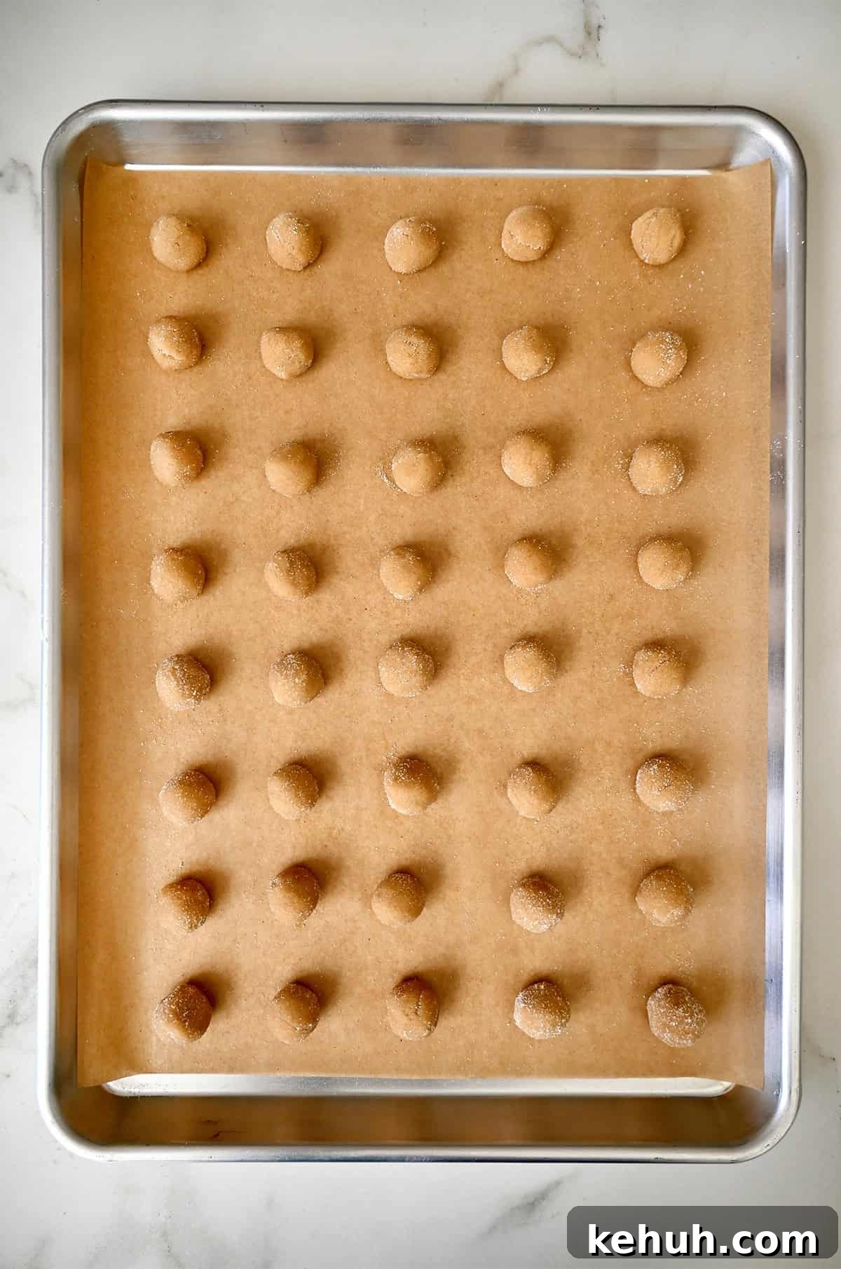 Mini peanut butter dough balls coated in sugar on a parchment paper-lined baking sheet.