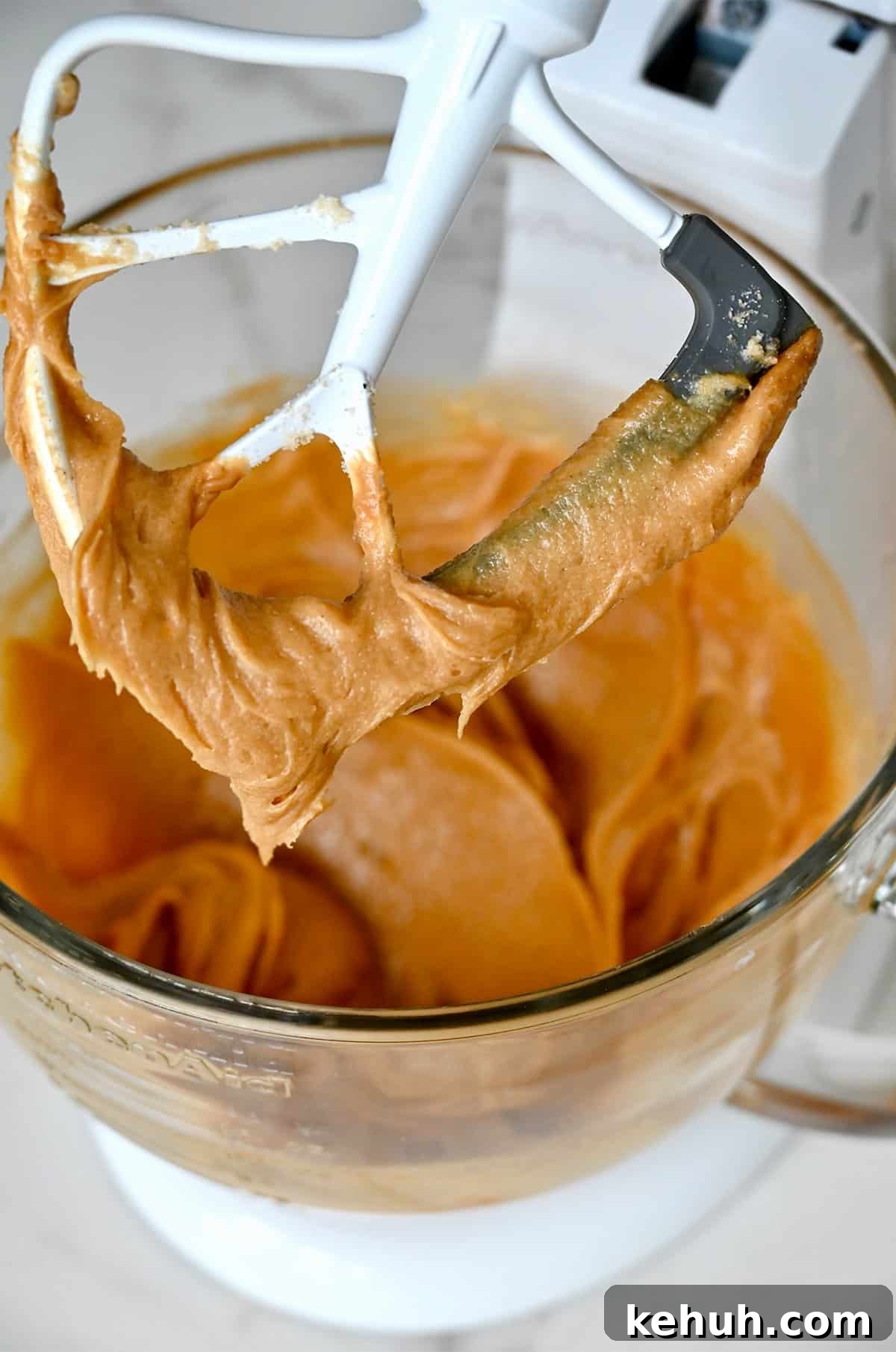 Peanut butter mixed with creamed butter, sugars, vanilla extract and eggs in the bowl of a stand mixer.