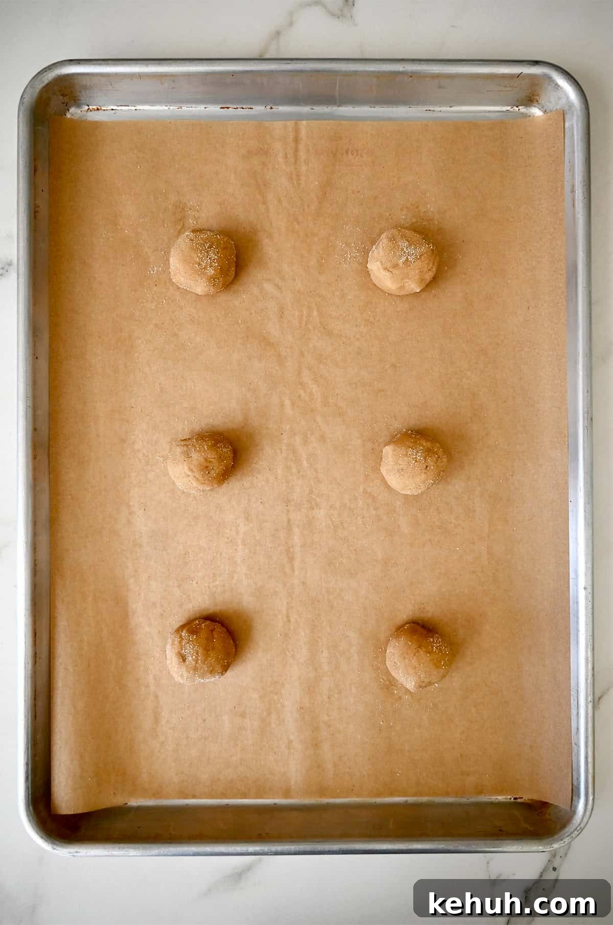 Peanut butter dough balls coated in sugar on a baking sheet lined with parchment paper.