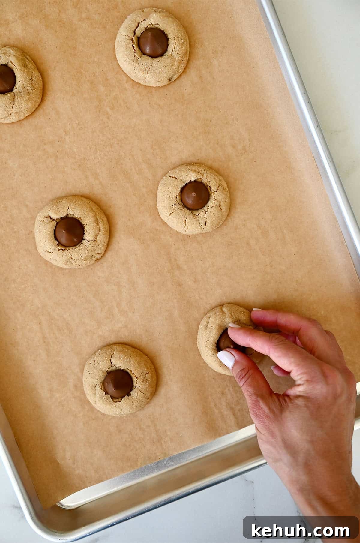 Pressing a chocolate kiss into warm peanut butter cookies to make peanut butter blossoms.