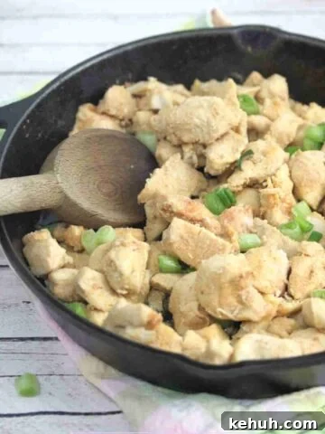 Spicy chicken bites in a cast iron skillet with green onions on top and a wooden spoon in the pan.