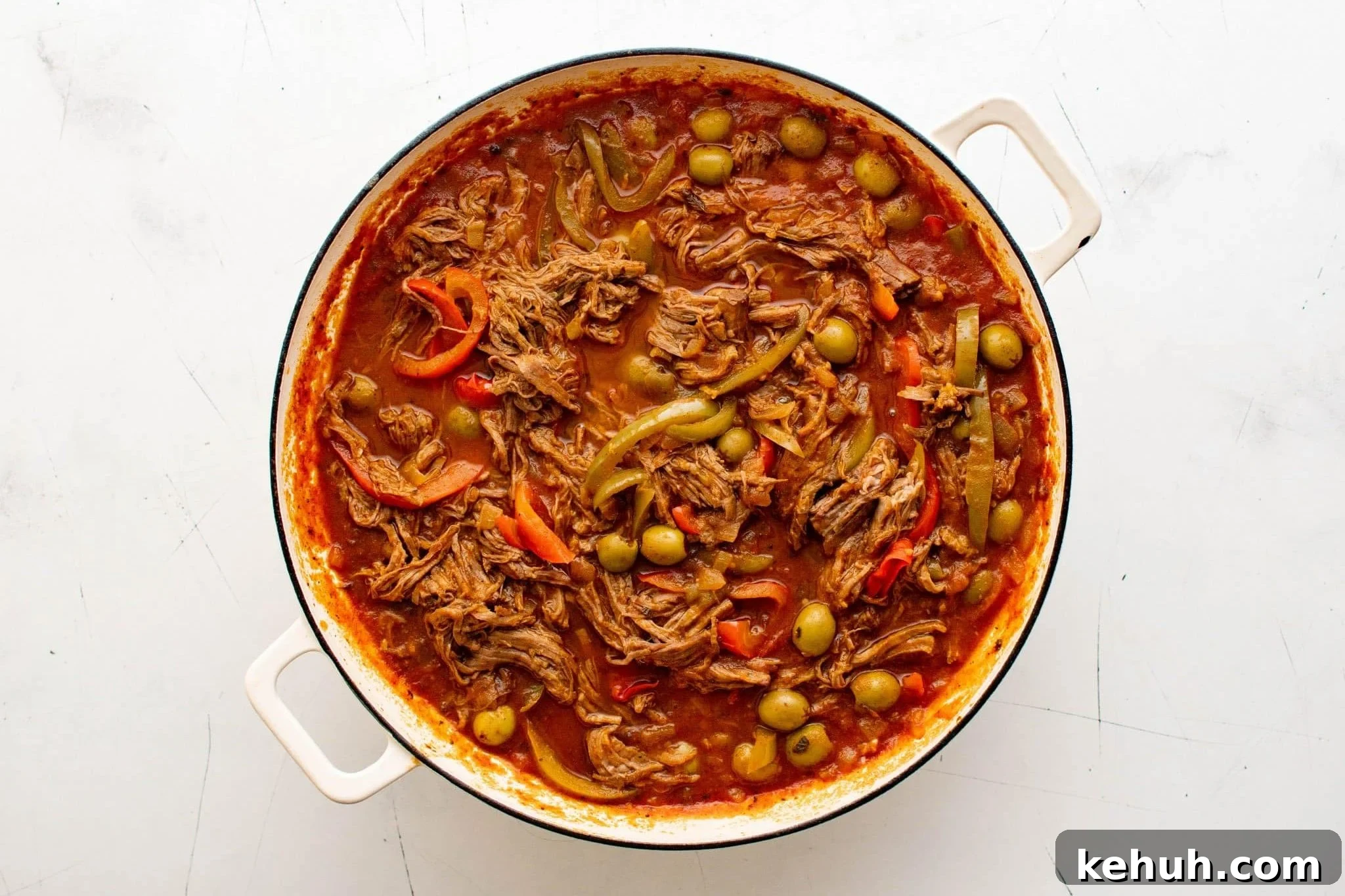 Authentic Cuban Ropa Vieja Recipe — Slow-Cooked Shredded Beef 11 Finished ropa vieja with shredded beef, peppers, and olives in a white Dutch oven.