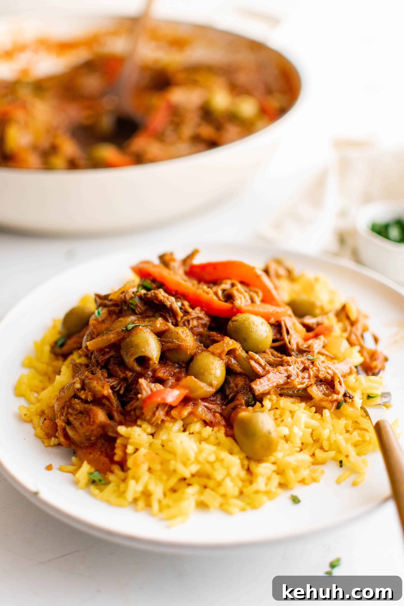 Authentic Cuban Ropa Vieja Recipe — Slow-Cooked Shredded Beef 12 White serving plate with yellow rice topped with cooked ropa vieja.