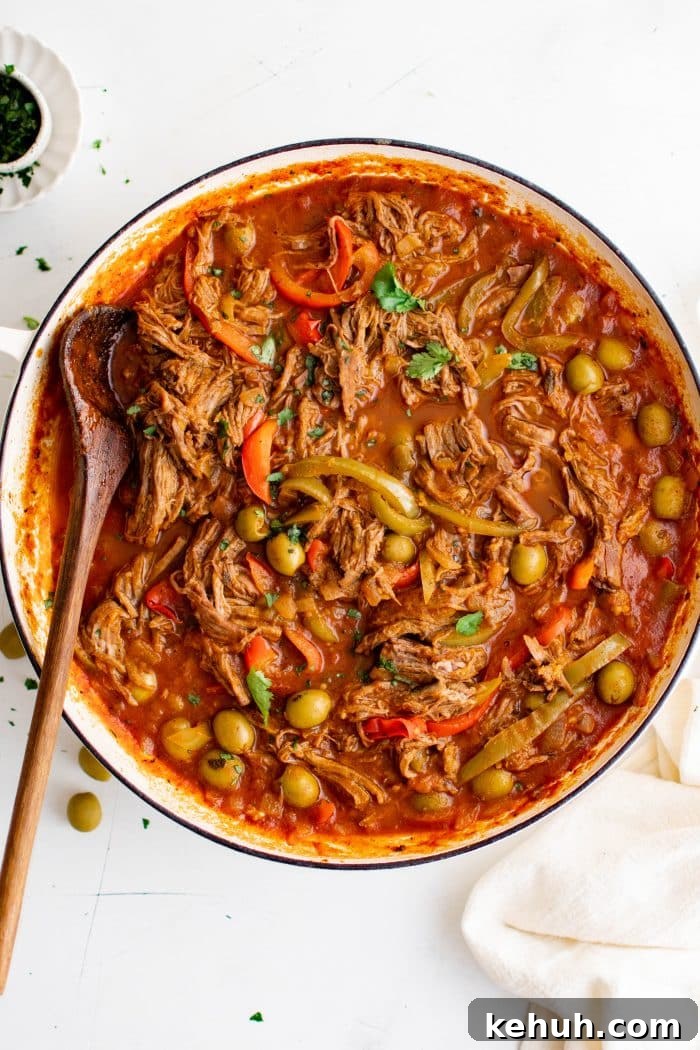 Authentic Cuban Ropa Vieja Recipe — Slow-Cooked Shredded Beef 17 Image of of shredded flank steak simmering with onions, bell peppers, and olives in a rich tomato sauce in a large Dutch oven.