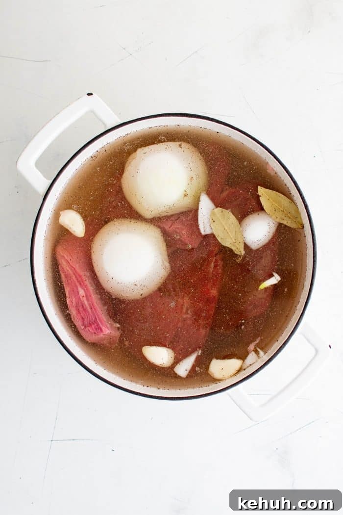 Authentic Cuban Ropa Vieja Recipe — Slow-Cooked Shredded Beef 4 Large white pot filled with flank steak, onions, garlic, bay leaves, and broth for ropa vieja.