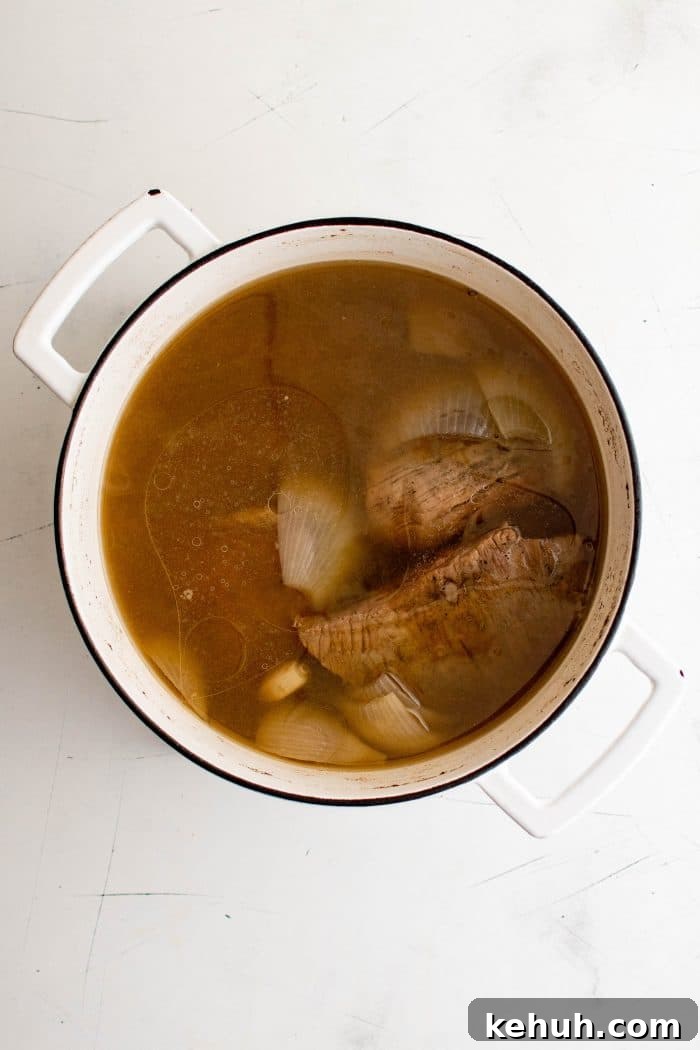 Authentic Cuban Ropa Vieja Recipe — Slow-Cooked Shredded Beef 5 Cooked flank steak resting in a pot of rich broth with soft onions and garlic.