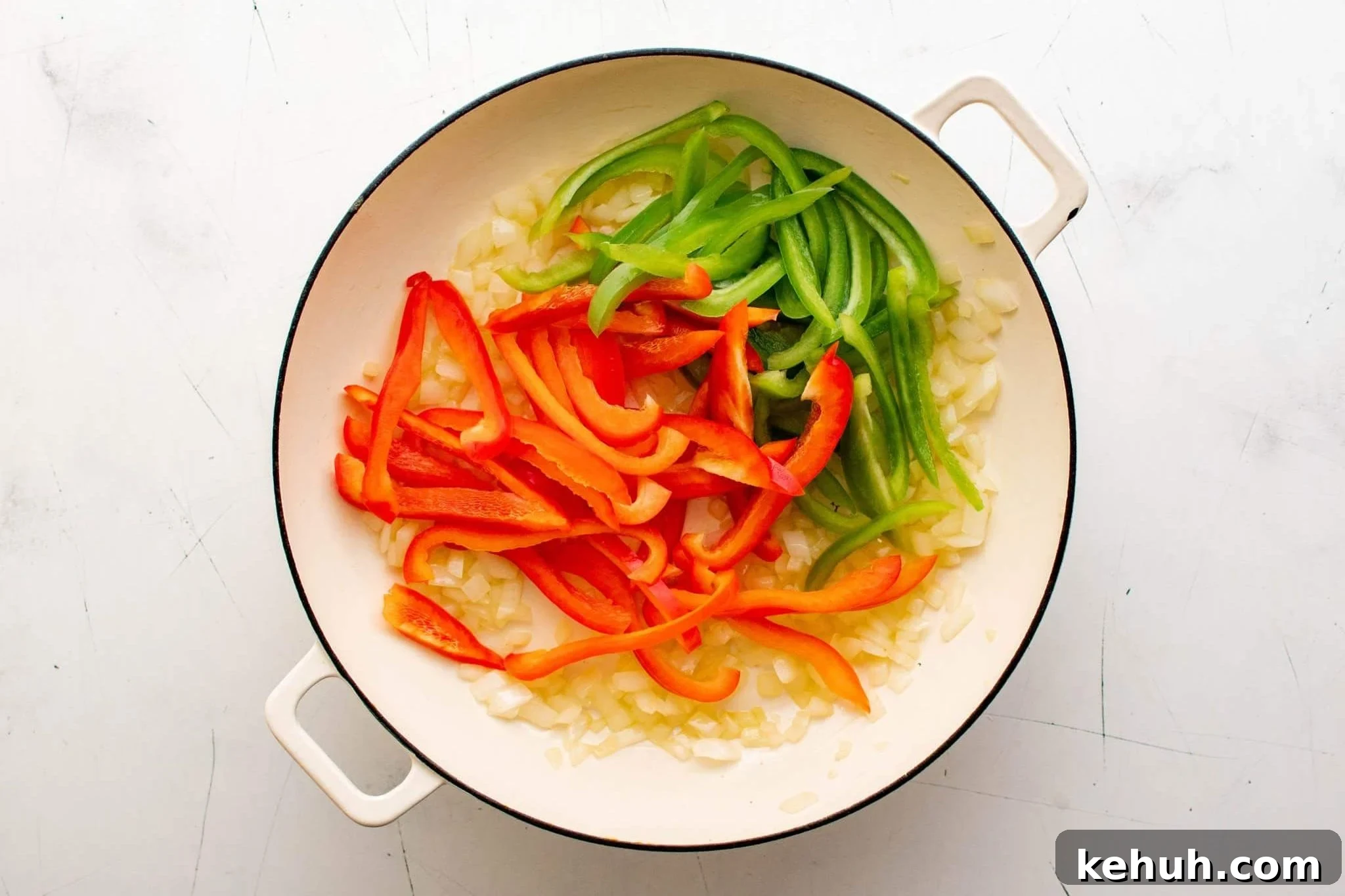 Authentic Cuban Ropa Vieja Recipe — Slow-Cooked Shredded Beef 7 Sliced red and green bell peppers added to sautéed onions in a white skillet.