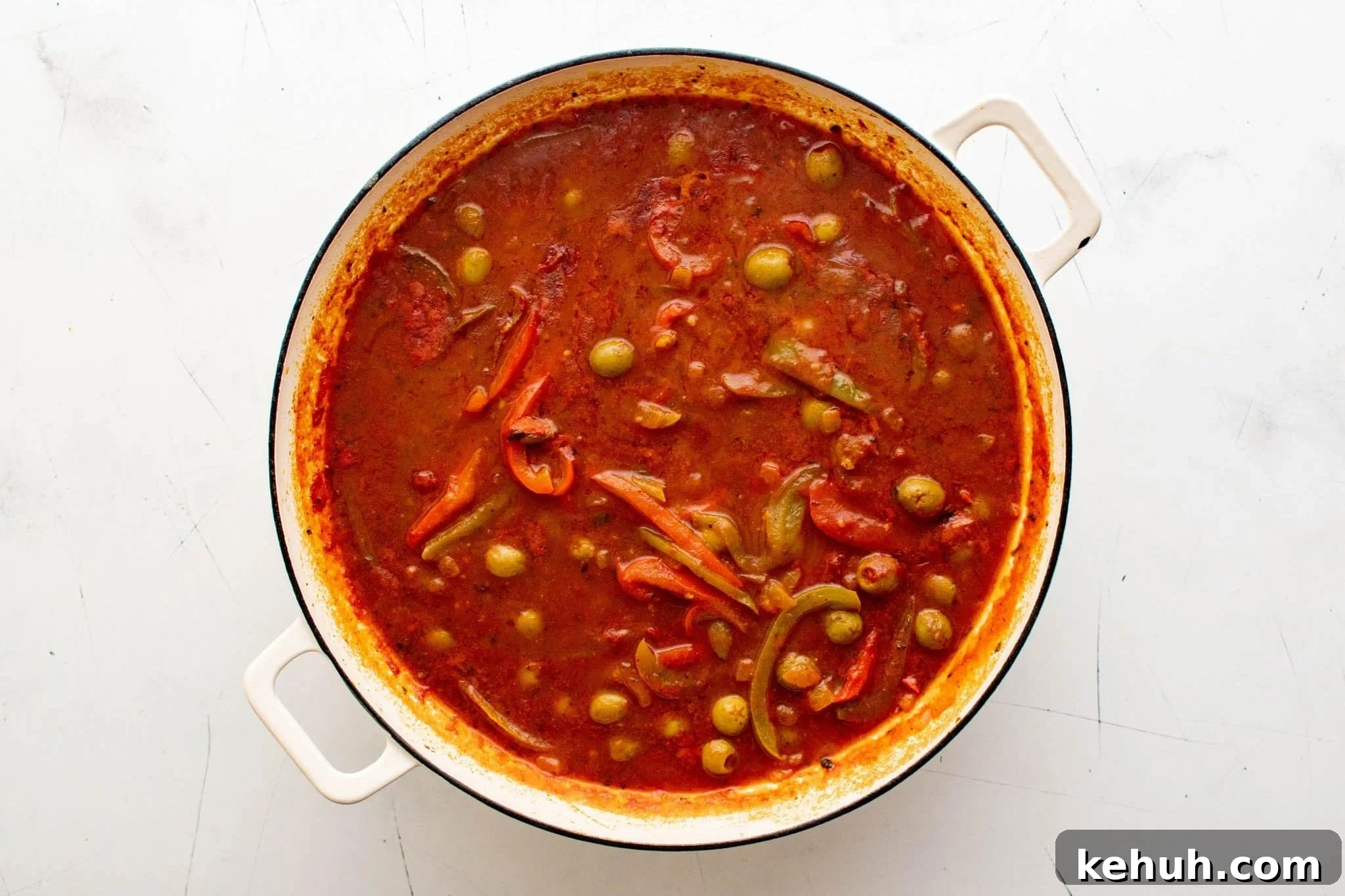 Authentic Cuban Ropa Vieja Recipe — Slow-Cooked Shredded Beef 9 Dutch oven filled with tomato sauce, peppers, and green olives simmering for ropa vieja.