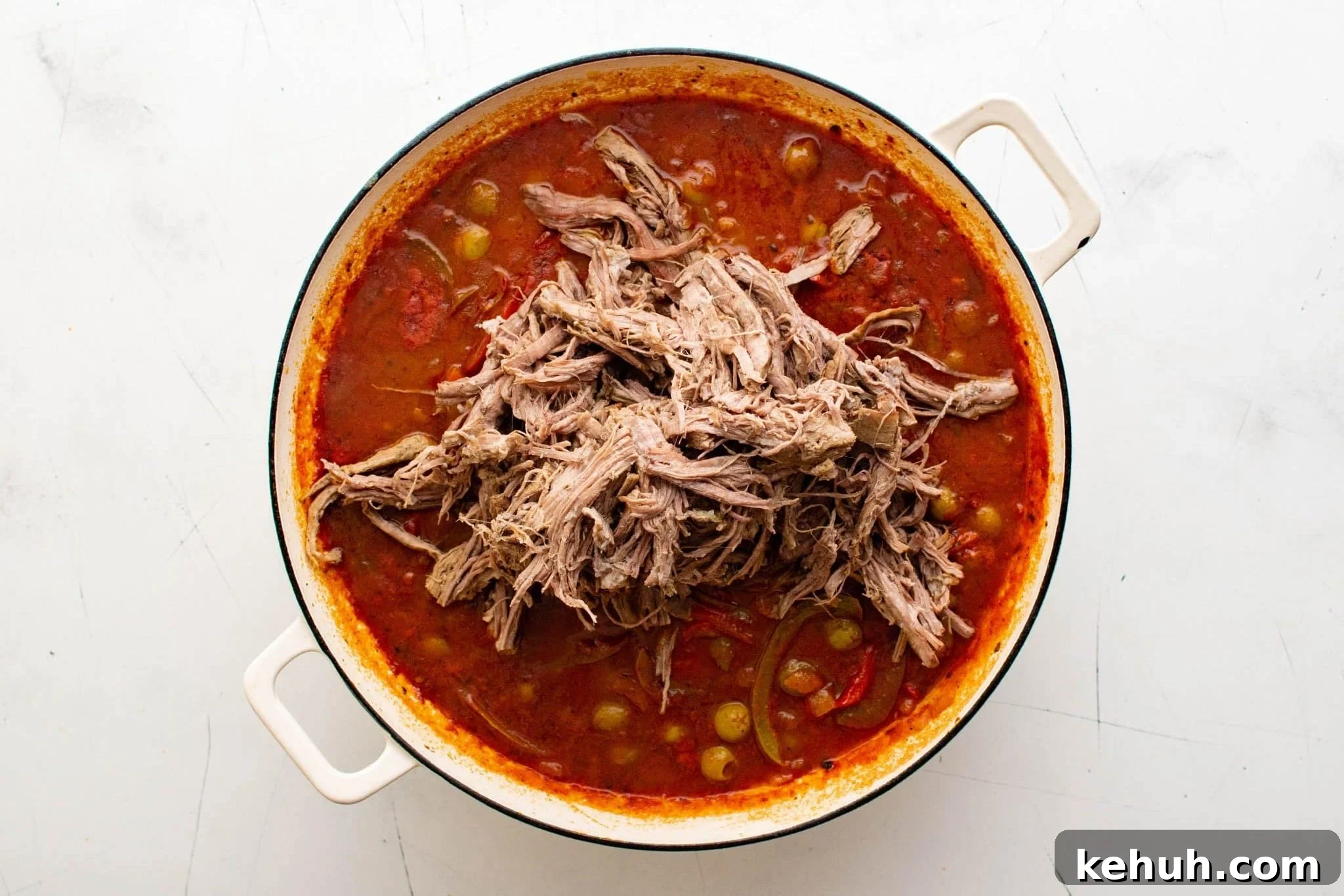 Authentic Cuban Ropa Vieja Recipe — Slow-Cooked Shredded Beef 10 Pile of shredded beef sitting on top of tomato and olive sauce in a Dutch oven.