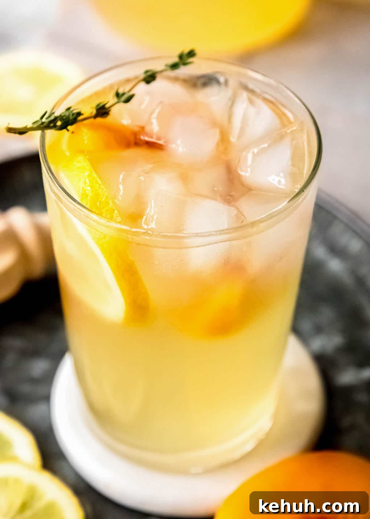 Peach Bourbon Lemonade Recipe — Refreshing Summer Cocktail 2 A glass of peach bourbon lemonade on ice, garnished with lemon and peach slices and a spring of thyme