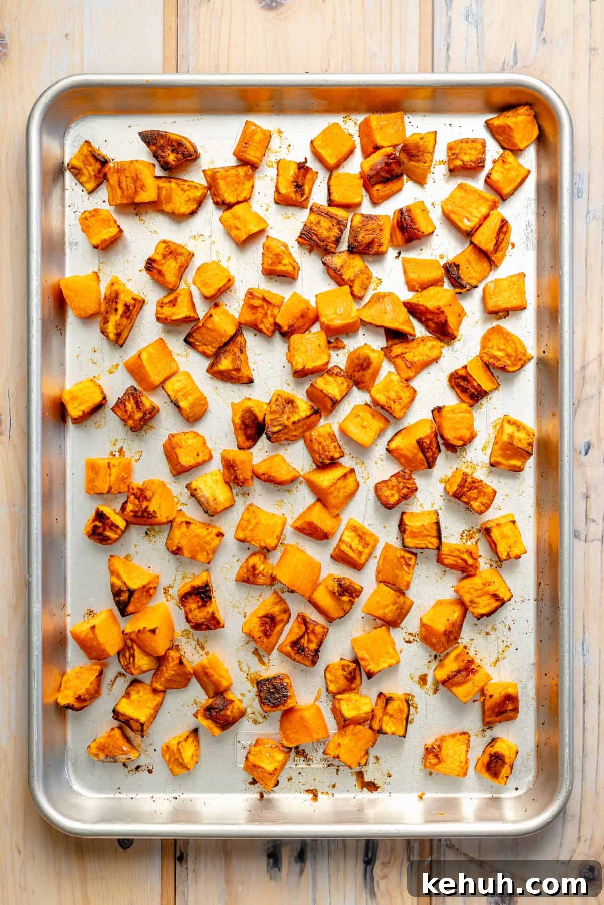 Street Corn & Sweet Potato Beef Bowl Recipe — Flavor-Packed Meal 4 Roasted sweet potato cubes spread evenly on a metal baking sheet, showing golden brown edges. The tray rests on a light wood surface.