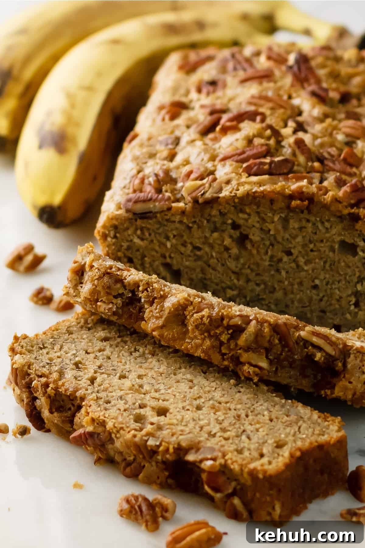 Dairy-free banana bread recipe sliced with ripe bananas in the background on a white table.