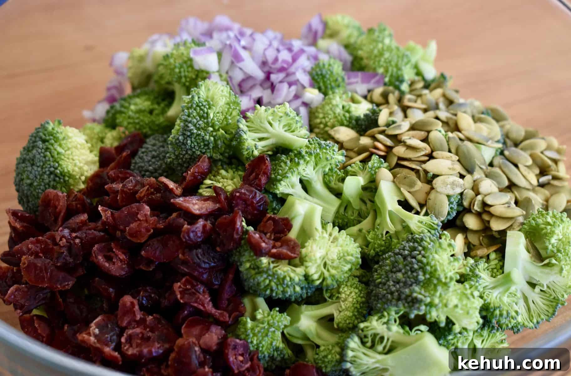 broccoli, cranberries, red onions, and sunflower seeds in a large glass bowl. 