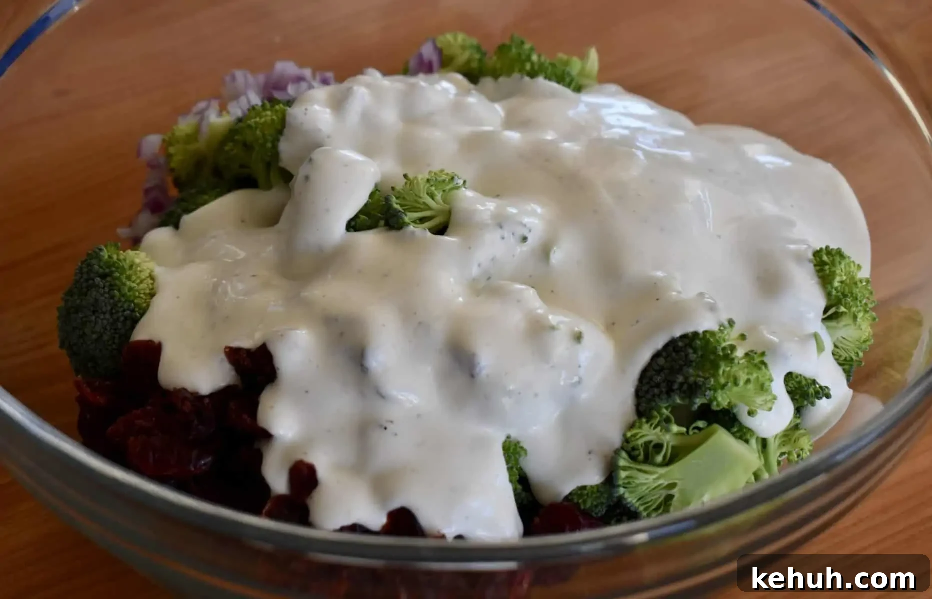 greek yogurt dressing poured over broccoli cranberry salad in a large glass bowl. 