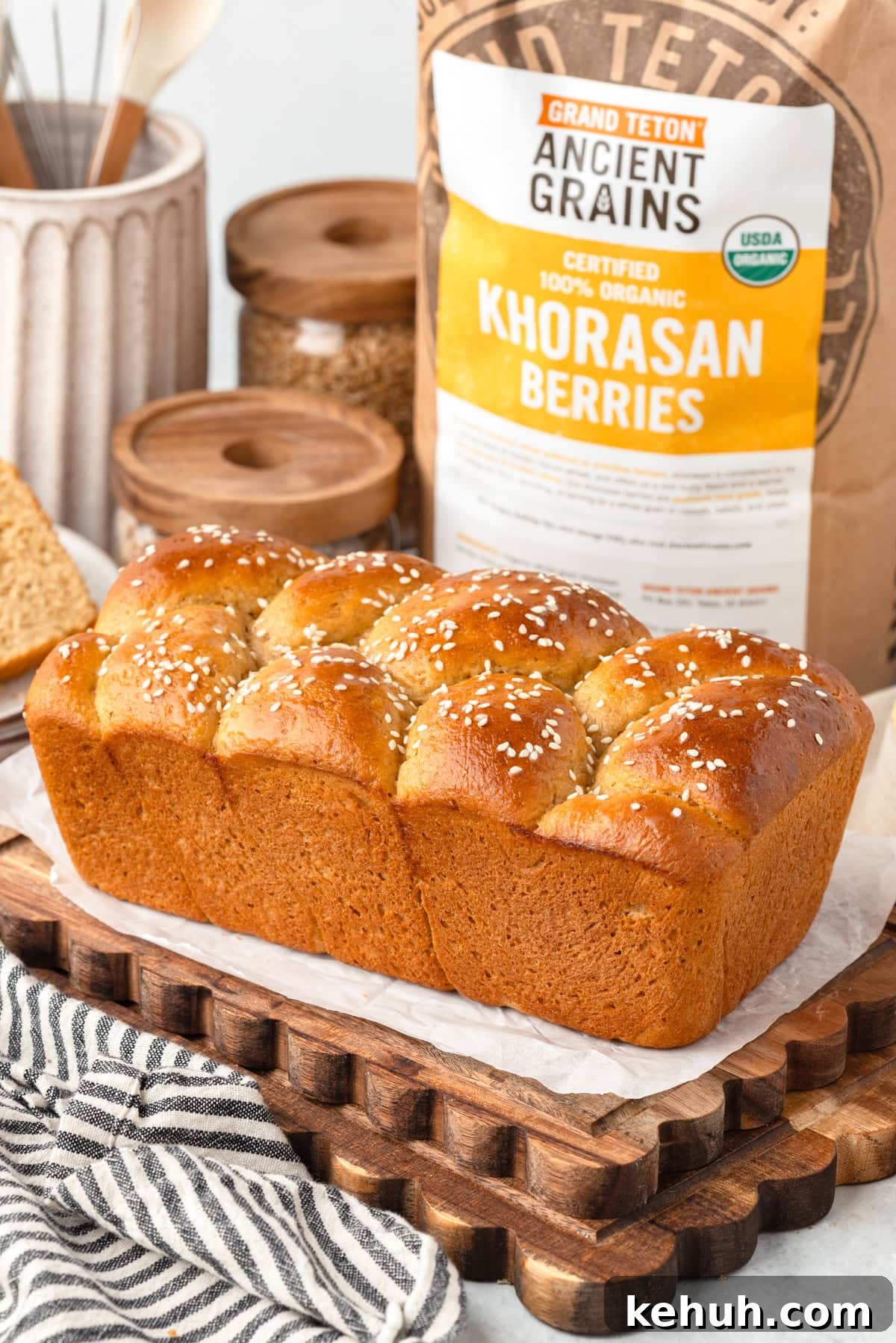 Braided sesame bread on a wooden tray with organic Khorasan berries bag, towel, and jar nearby.