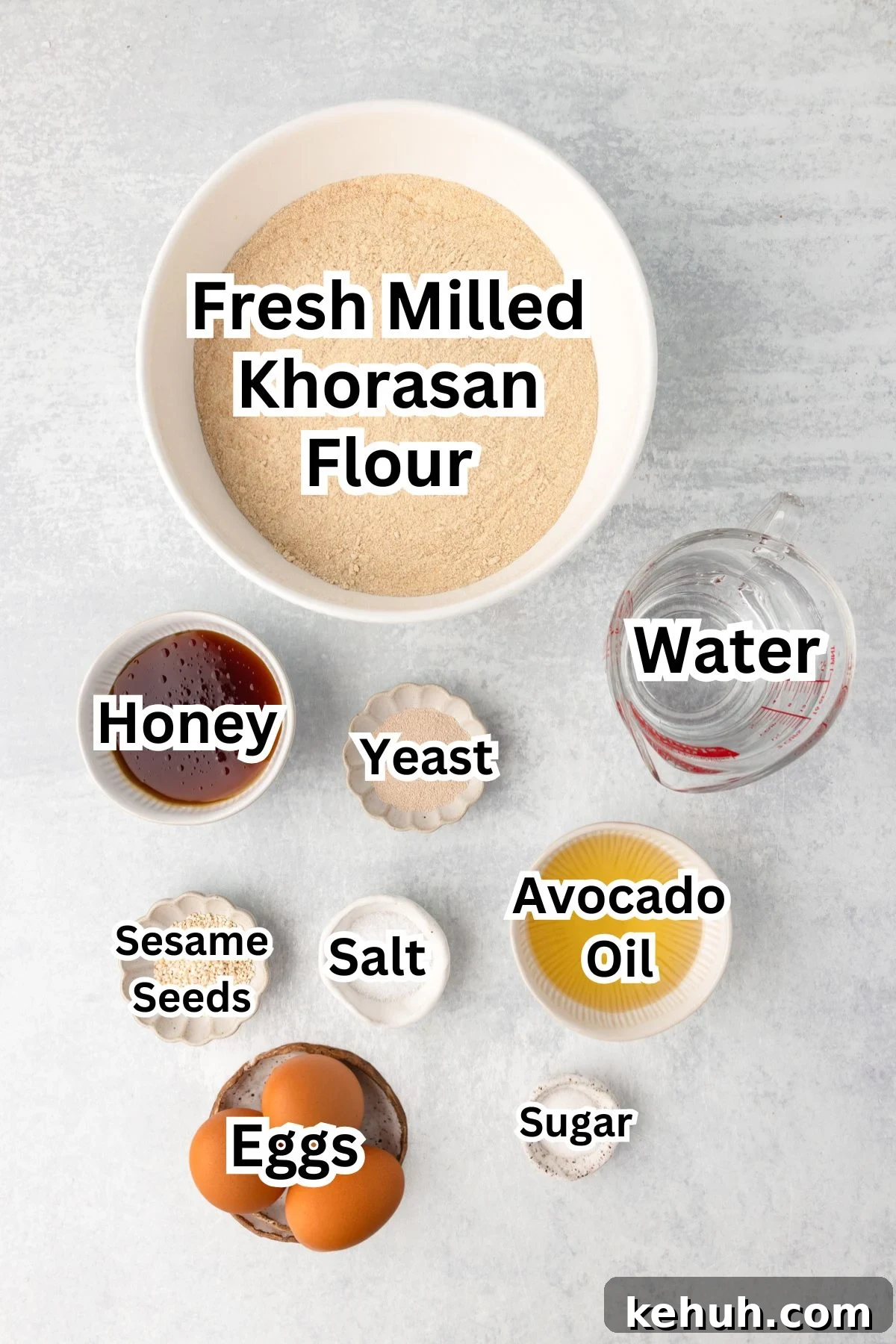 Top-down view of bowls containing measured baking ingredients, each labeled: flour, water, honey, oil, yeast, salt, eggs.