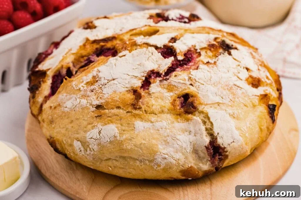 front close up image of baked sourdough bread with some flour on the top and the raspberries inside all on a wooden board.