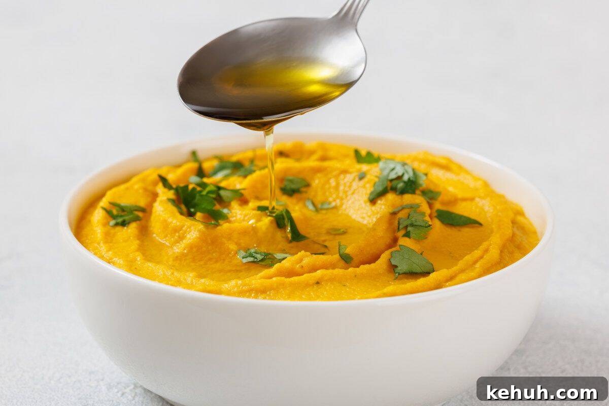 Bowl of Roasted Carrot Hummus garnished with green herbs, with a spoon drizzling oil above it.
