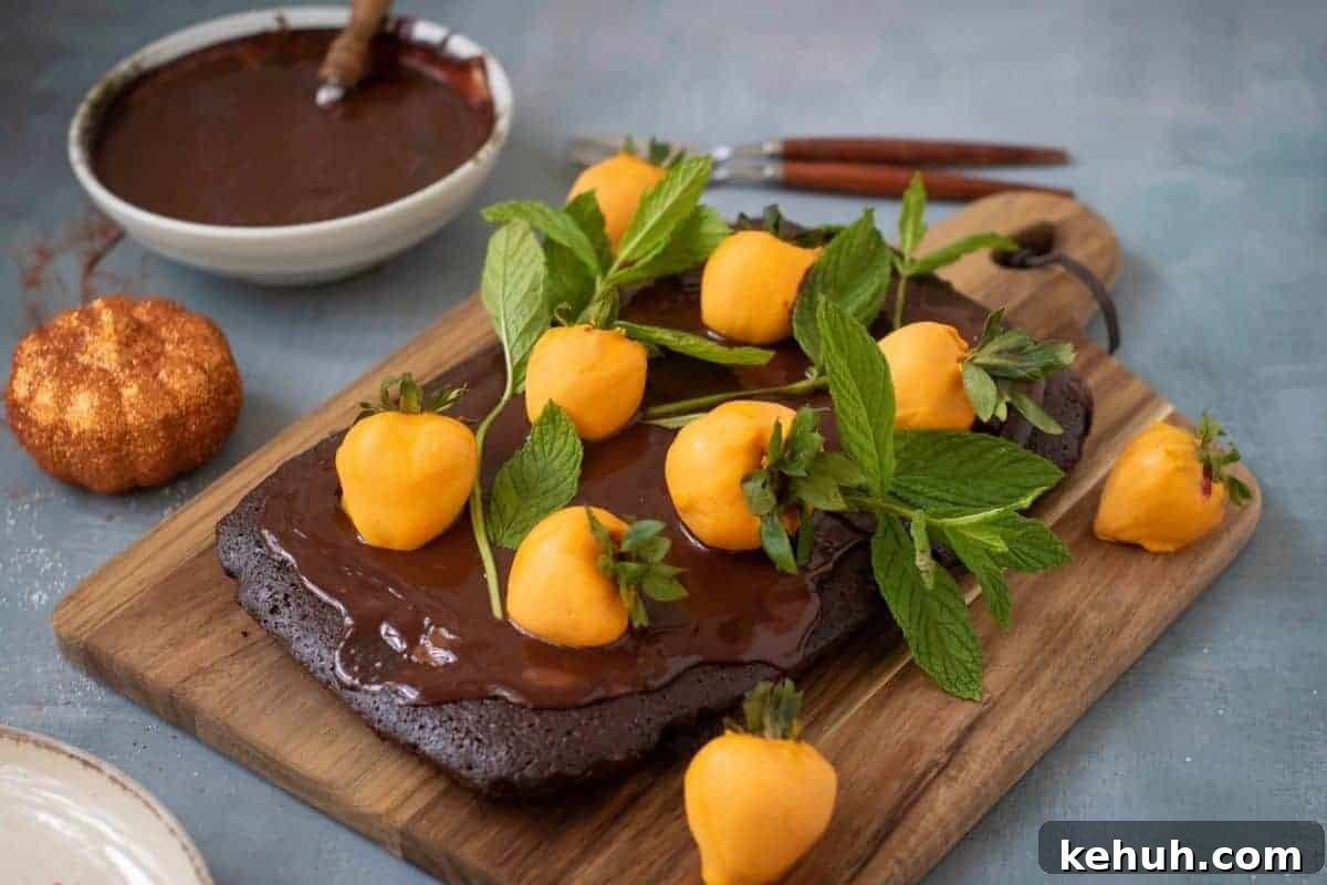 A rectangular Halloween Pumpkin Patch Brownie Cake, topped with yellow fruit resembling mini pumpkins and fresh mint, sits on a wooden board.